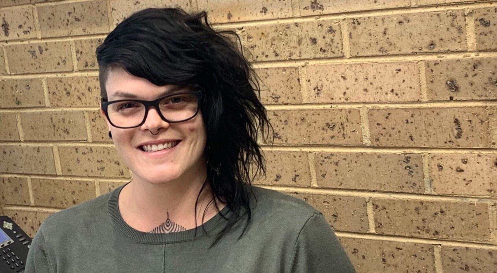 Photo of Lucie in her office. Lucie is smiling, wearing black glasses and a army green top.