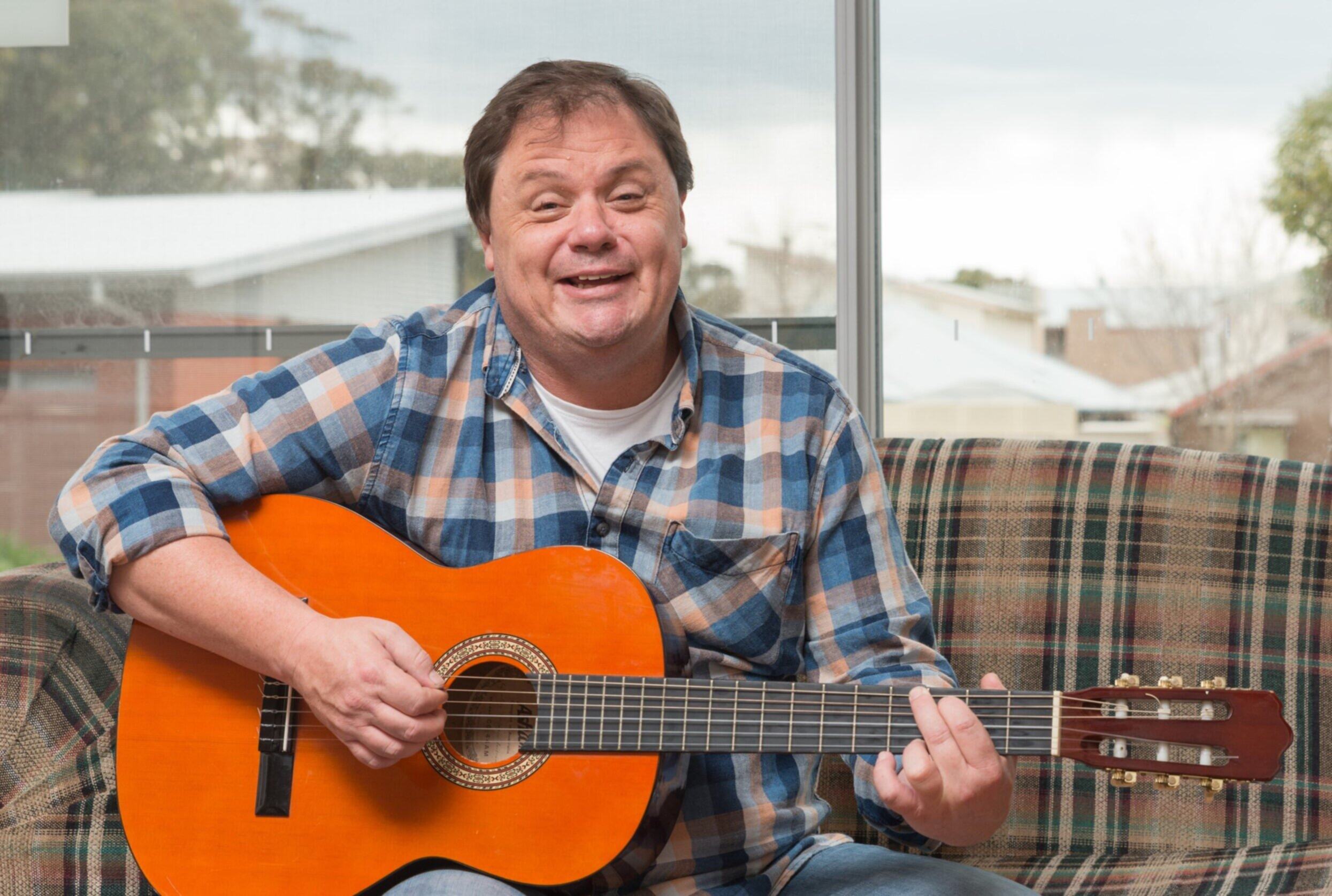 Paul is sitting on his balcony couch holding a guitar
