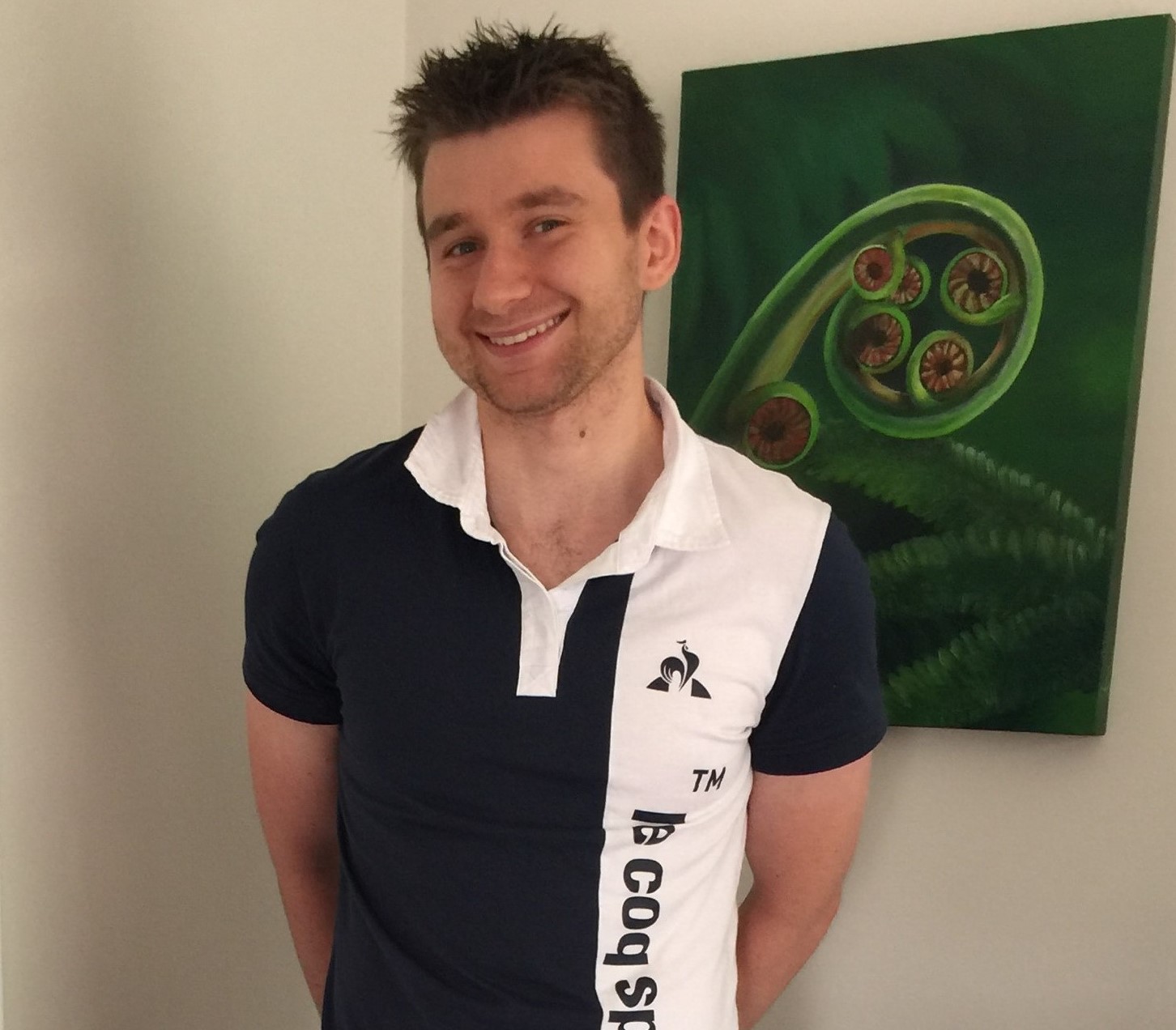 Isaac stands in a black and white polo shirt, smiling at the camera.