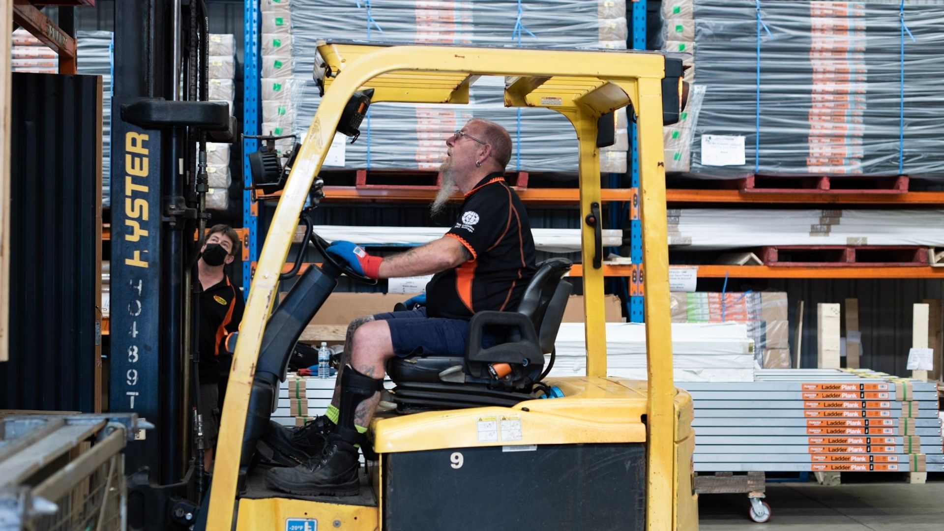 Charles is driving a forklift. He is wearing his Extreme Agencies uniform.