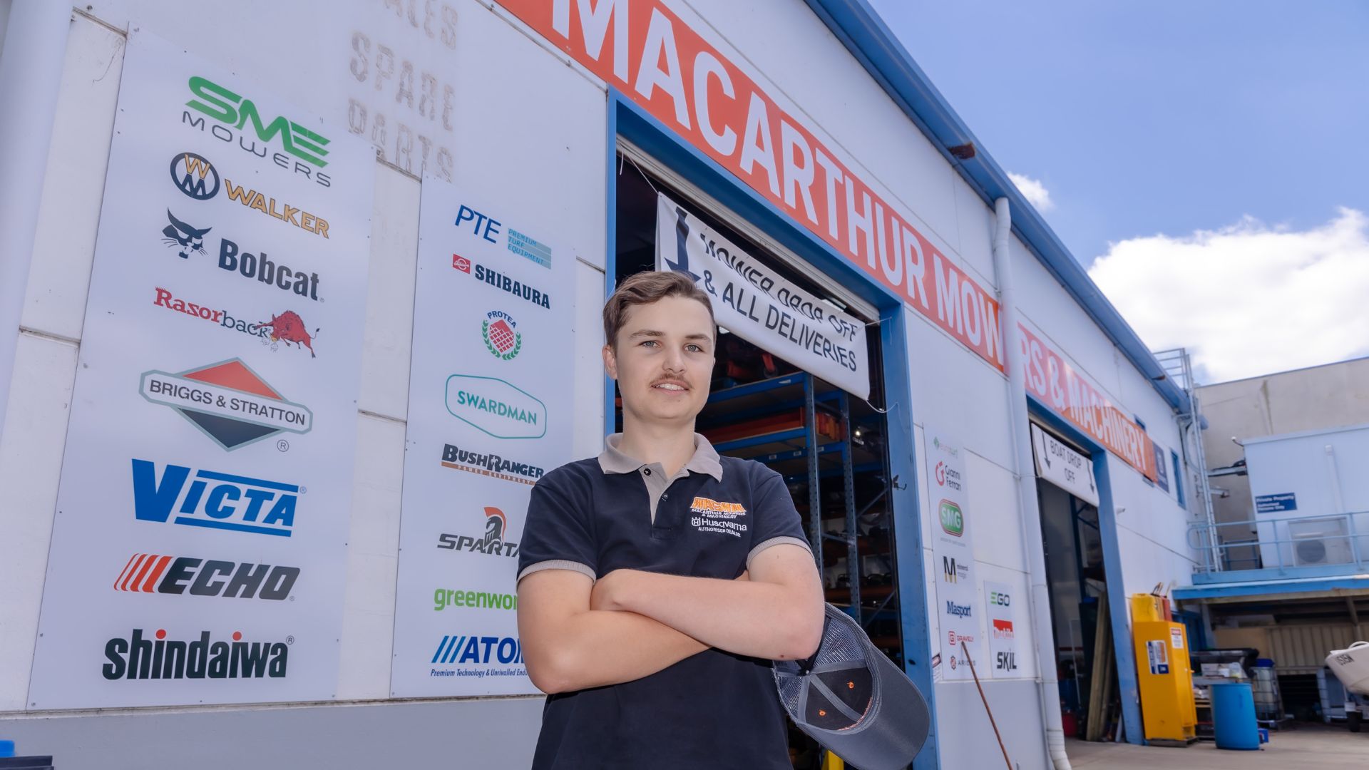 Ash standing with his arms crossed in front of Macarthur Mowers.