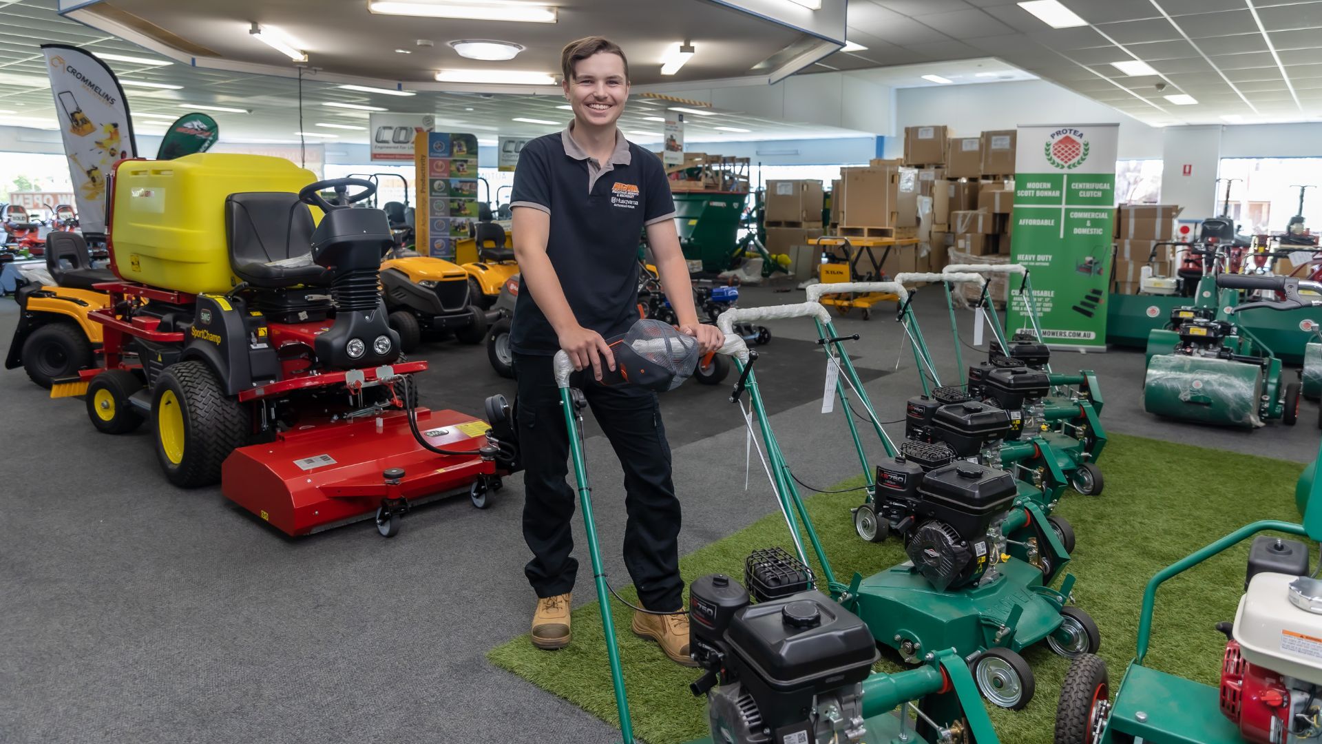 Ash standing with a lawn mower and smiling at the camera.