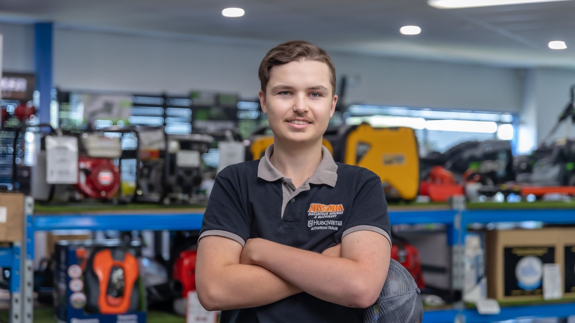 Ash standing with his arms crossed in front of Macarthur Mowers shelves.