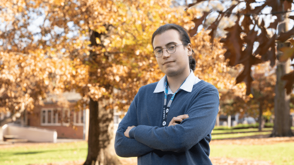 Robert is standing, arms crossed, in front of a tree with orange leaves
