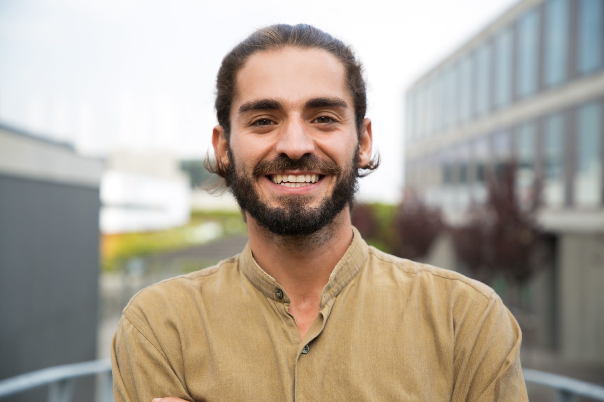 Cheerful young man with a beard smiling at the camera outdoors.