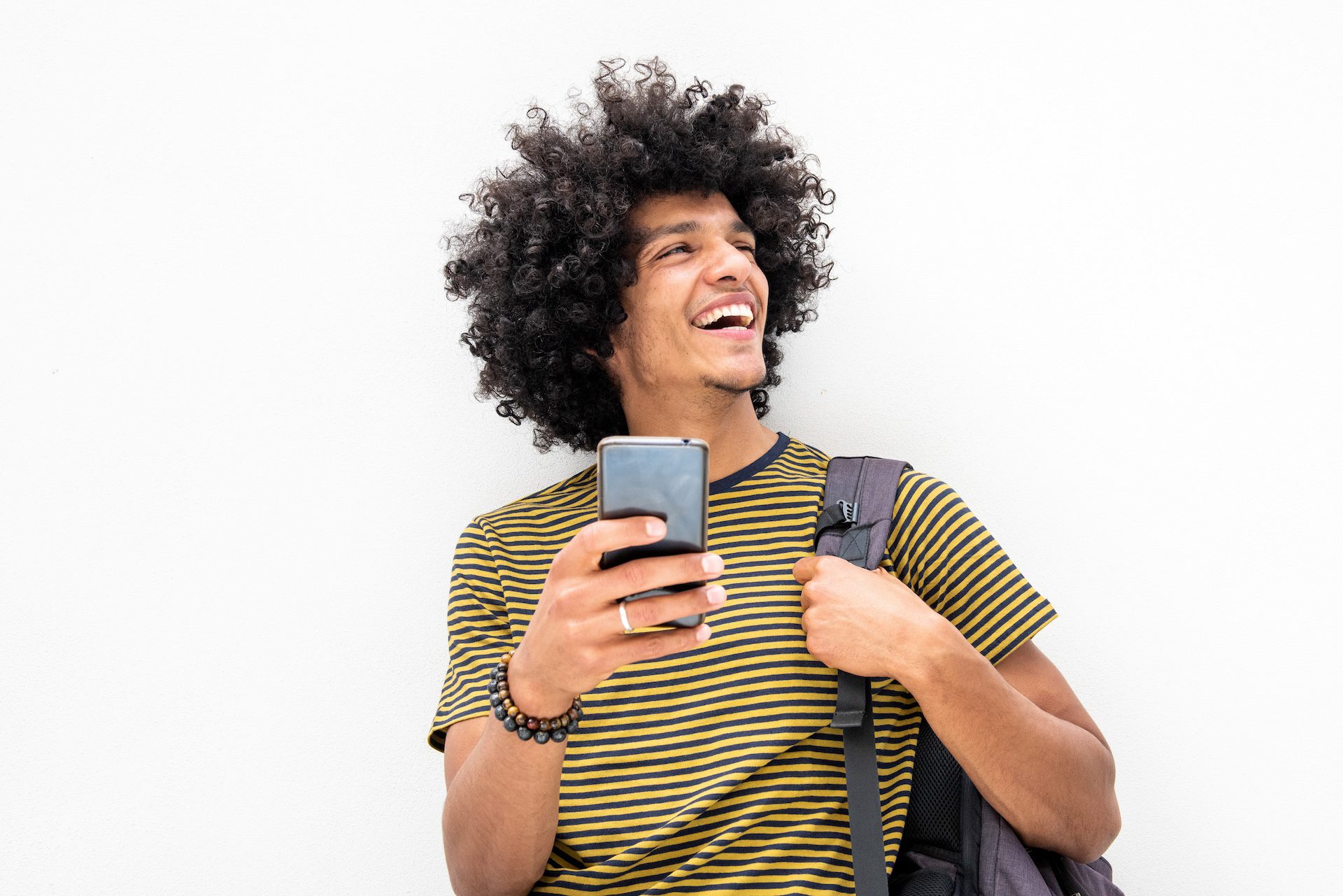 Portrait of a happy young man with a bag and cellphone, smiling against an isolated white background.