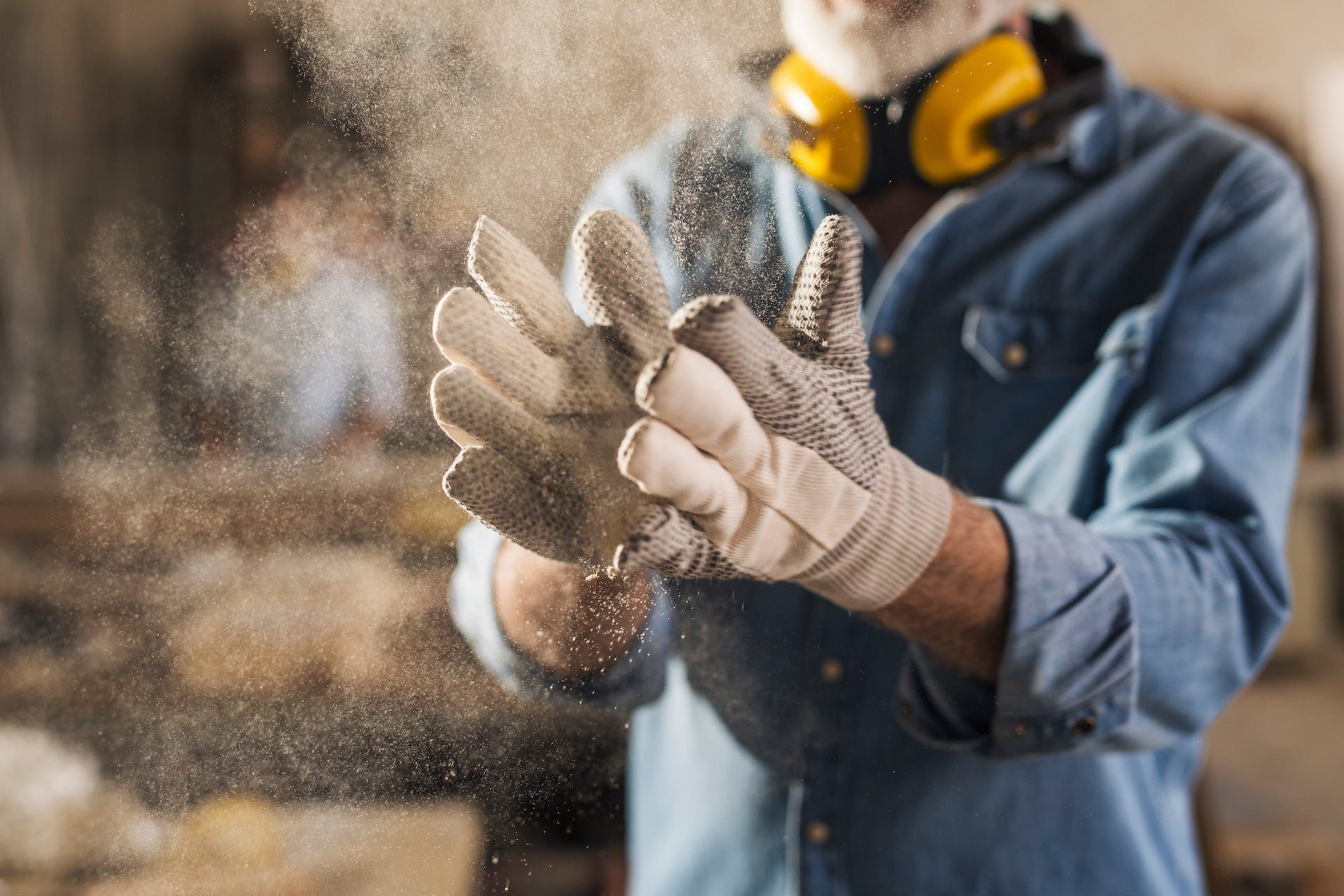 Unrecognizable male hands in work gloves clapping to remove sawdust.