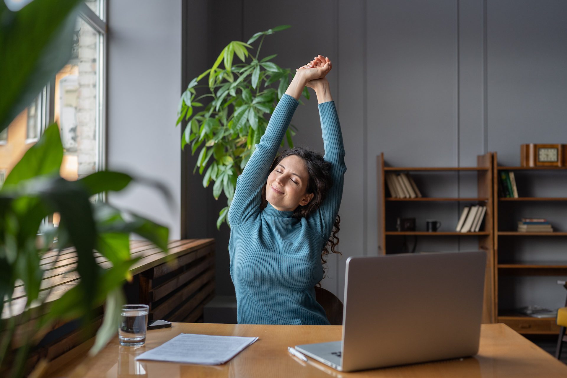 Happy businesswoman stretching at her workplace, taking a break from the computer screen.