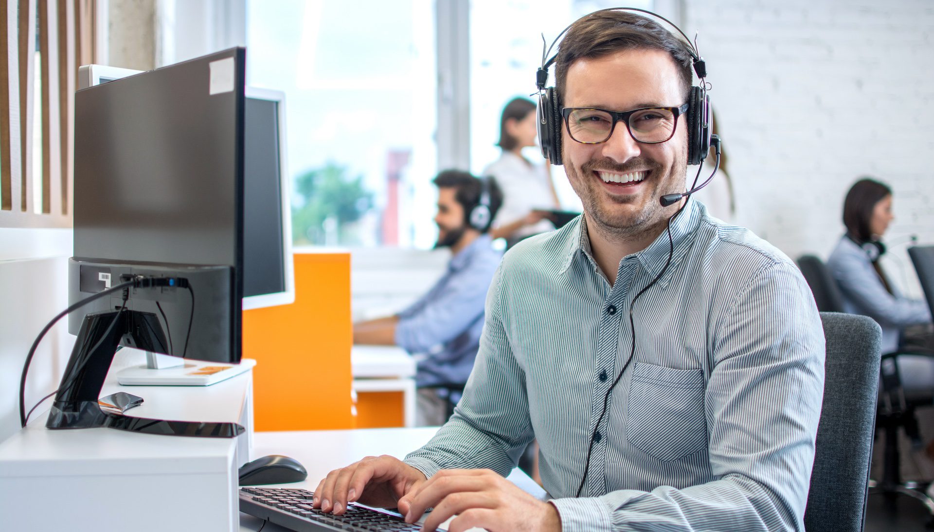Young male technical support dispatcher in a call center, wearing a headset and assisting a customer.