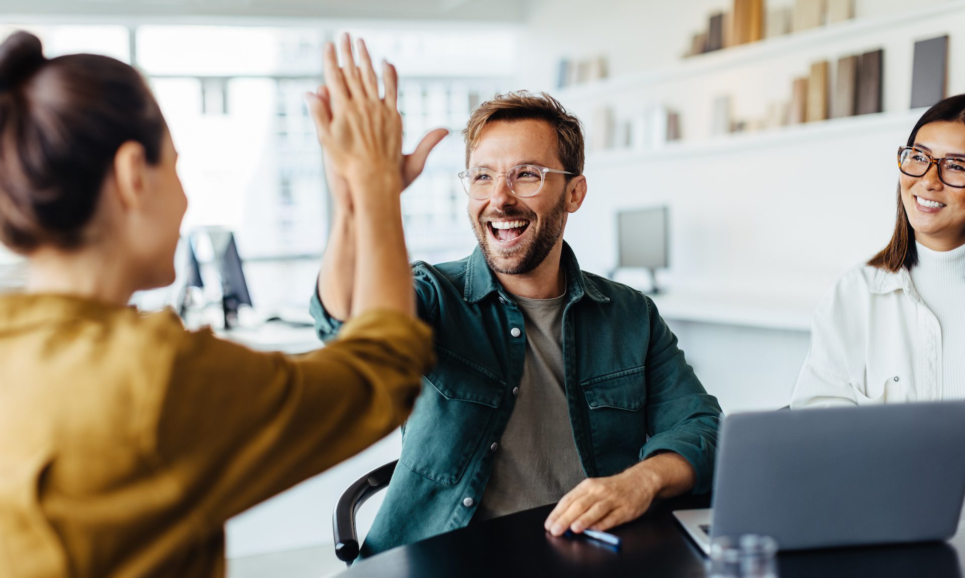 Successful young business professionals giving each other a high five to celebrate teamwork in a meeting.