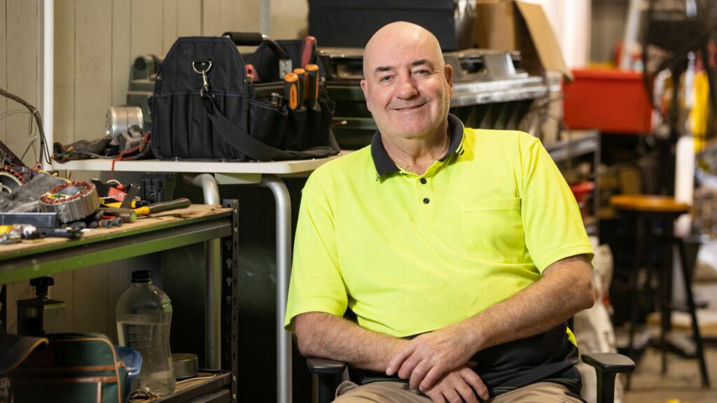 Middle-aged man sitting in a messy electrical workshop.