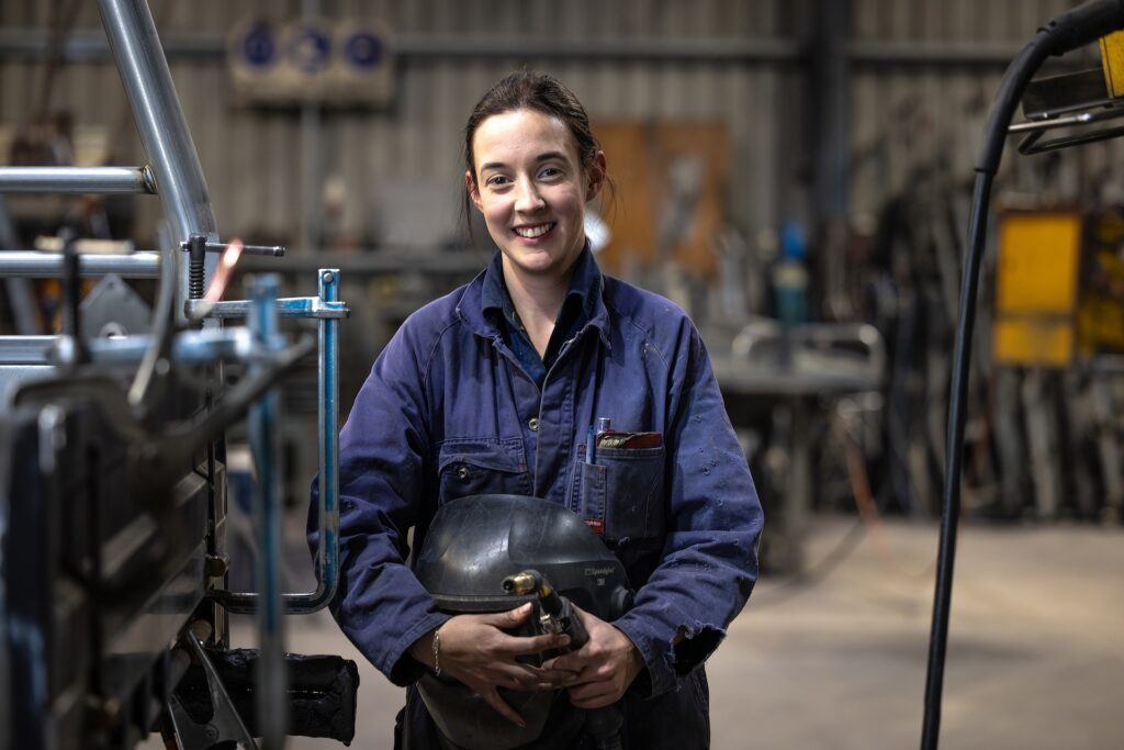 Woman smiling while holding welding equipment in a workshop.