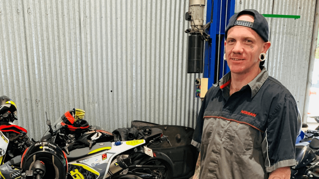 A male Nissan employee posing with motorcycles in a repair shop.