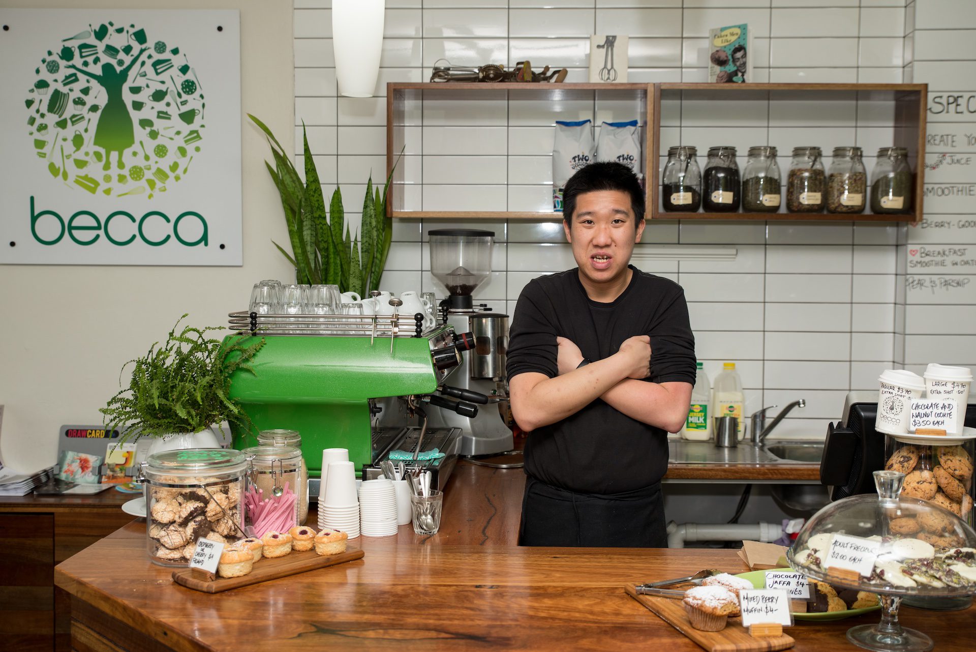 Young Asian man standing behind a cafe counter.