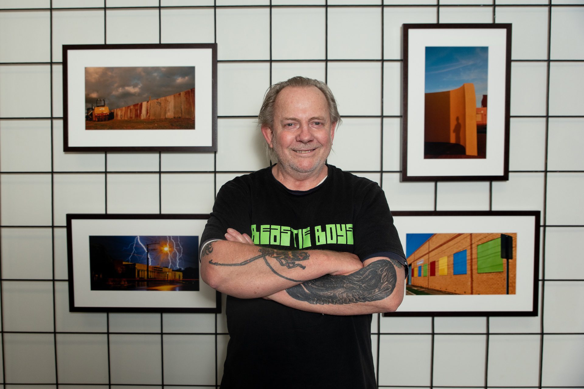 Middle-aged man standing with arms crossed in front of a wall with paintings.