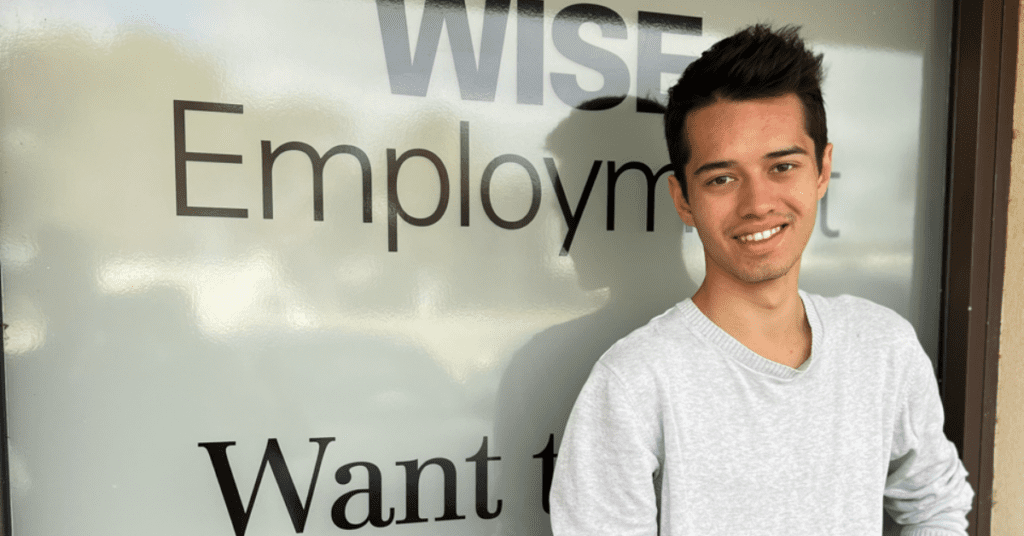 A smiling young man standing in front of an employment office.