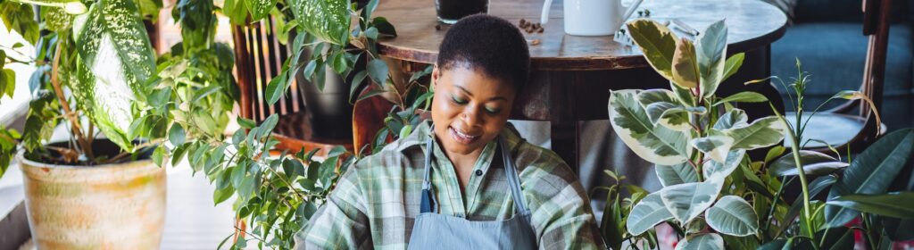 Young African American woman gardening, repotting plants and caring for flowers.