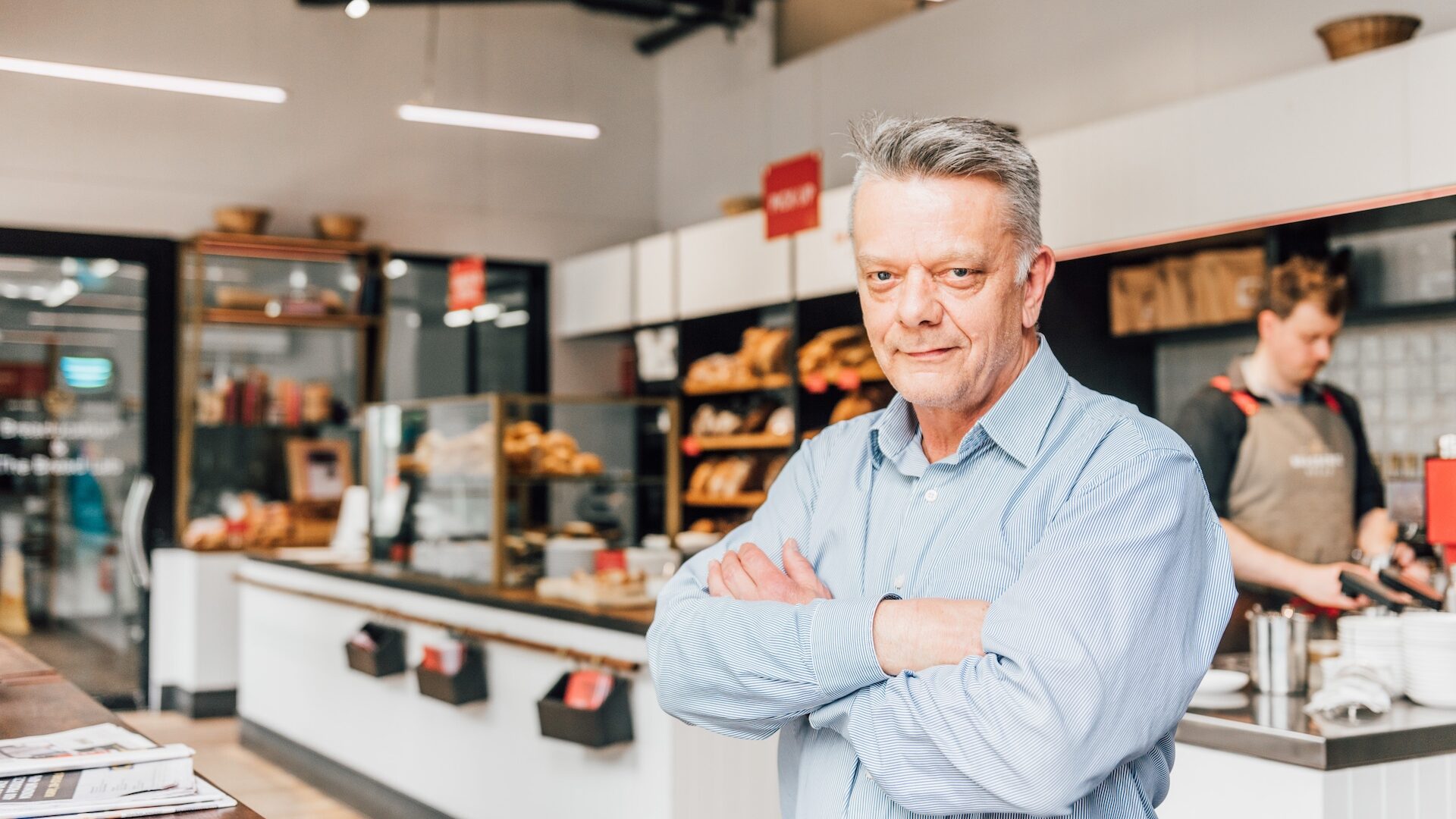 Man standing with arms crossed in front of a bakery counter.