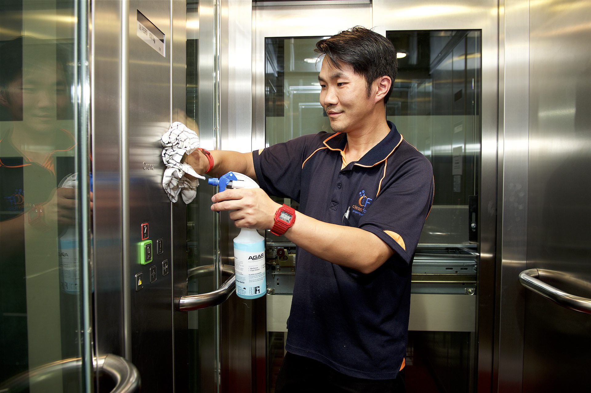 Asian man with a spray bottle, cleaning the walls of an elevator.