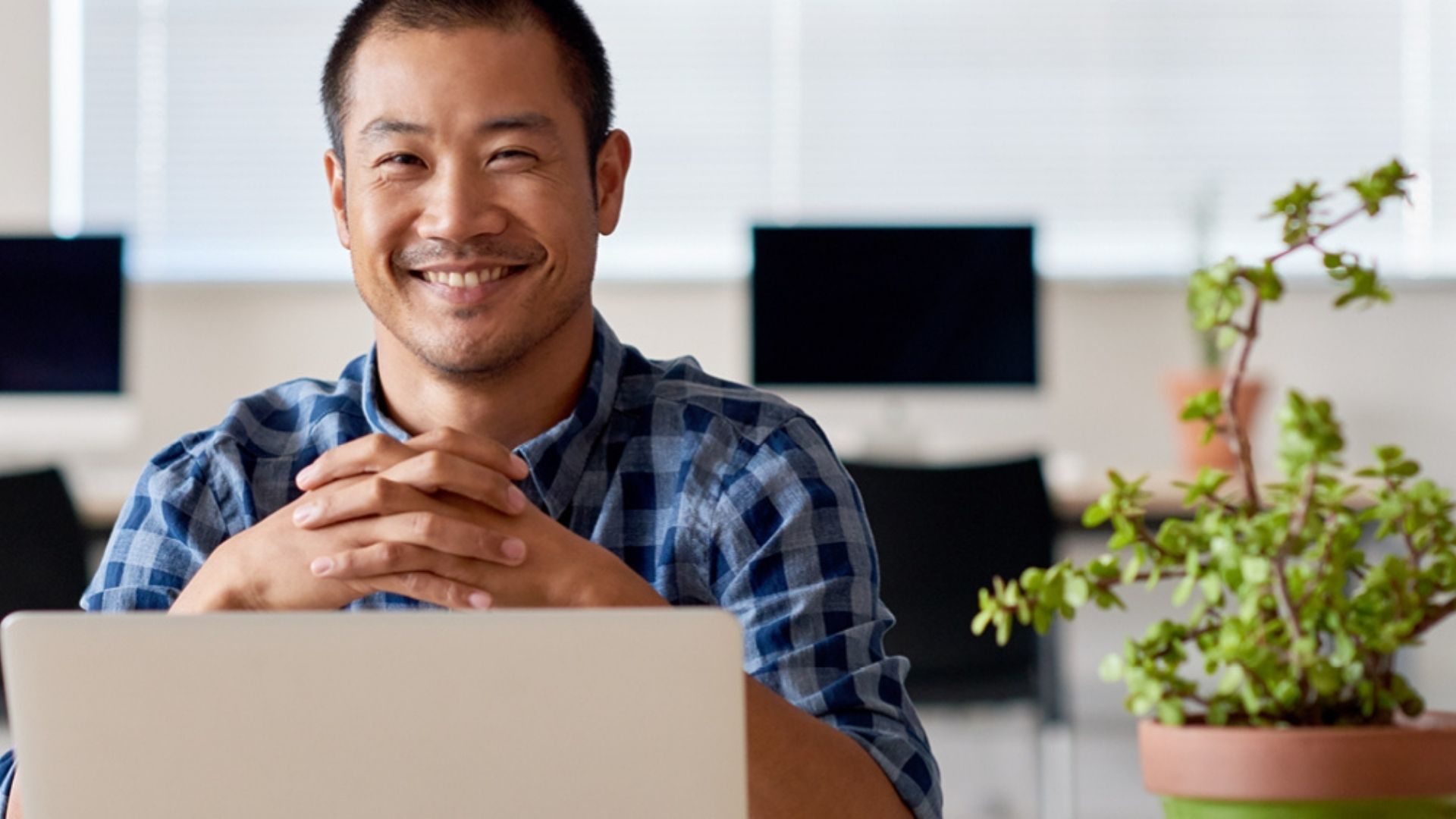 Smiling Asian man, sitting in front of a laptop.