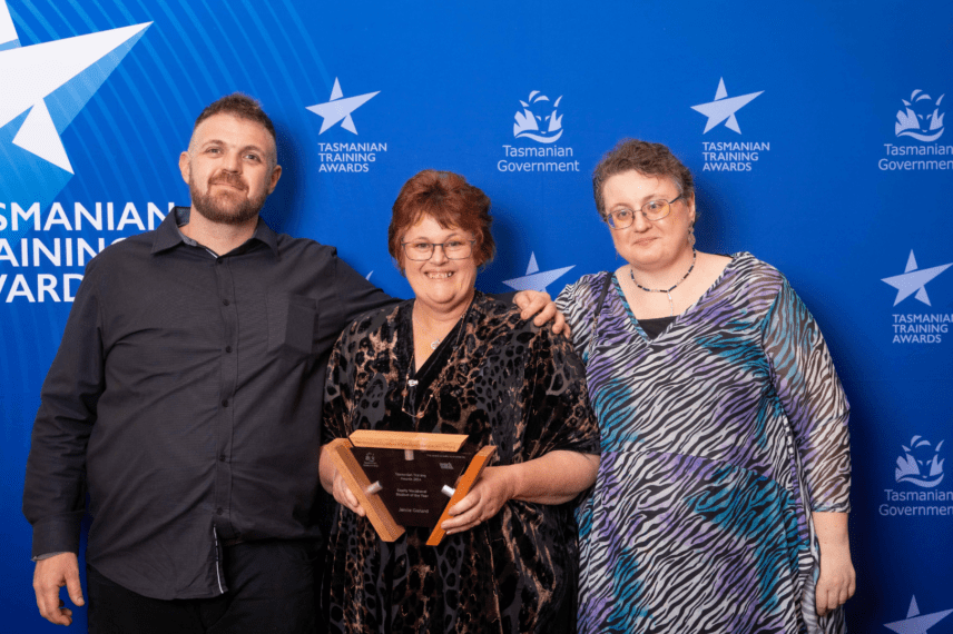 Jennie Garland in between a young man and woman, holding a trophy