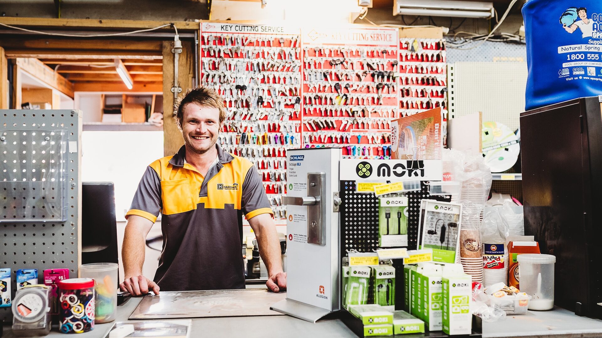A young man smiling while standing behind a key duplication counter.