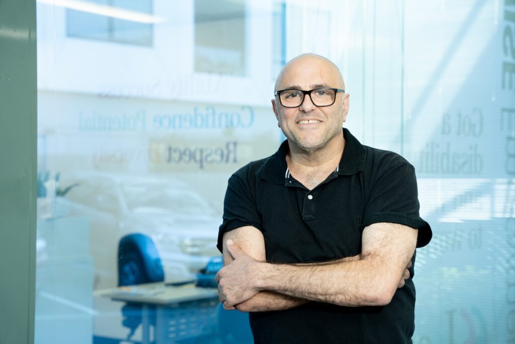 Smiling man with arms crossed standing in front of an office.