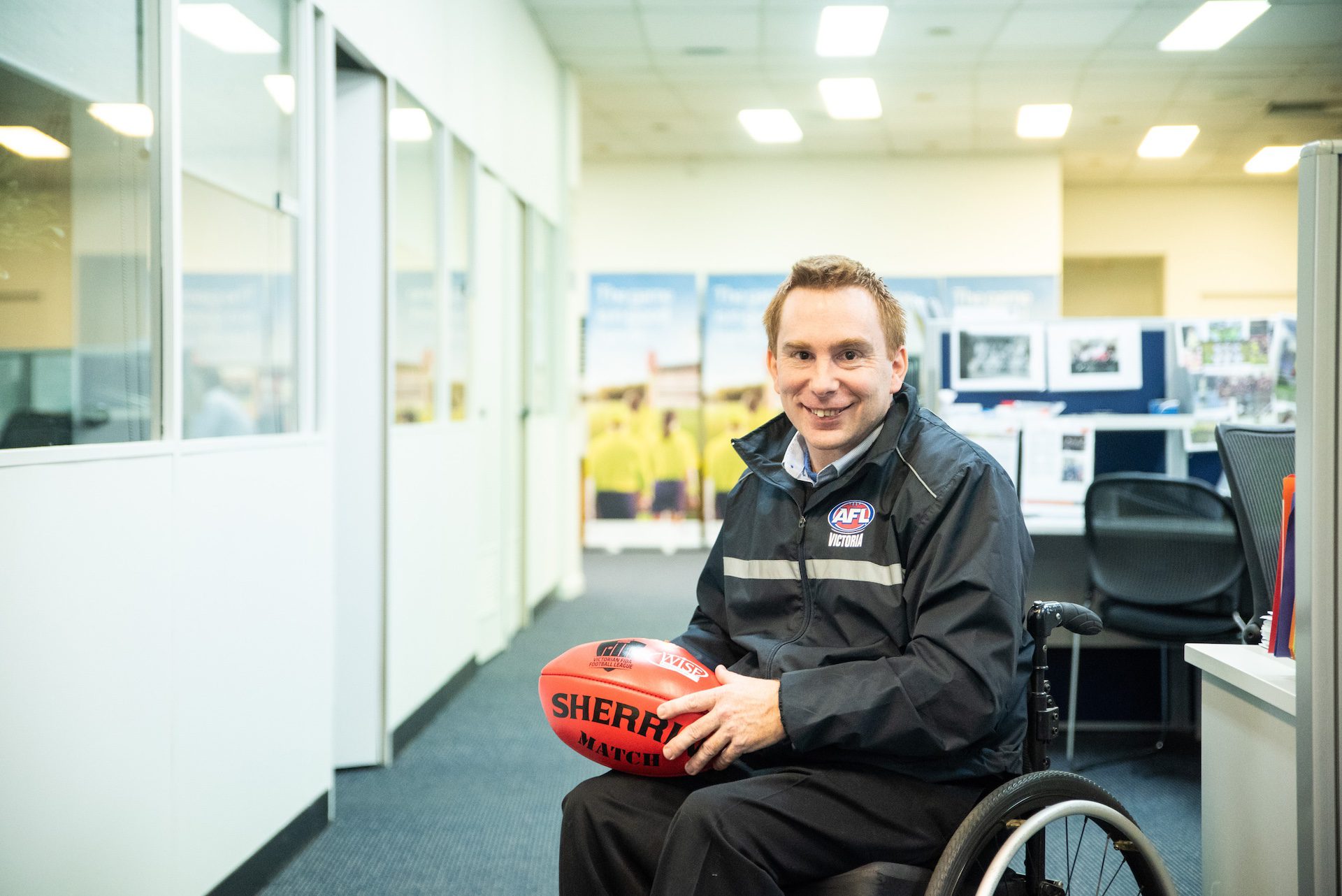 Man in a wheelchair holding a football in an office.