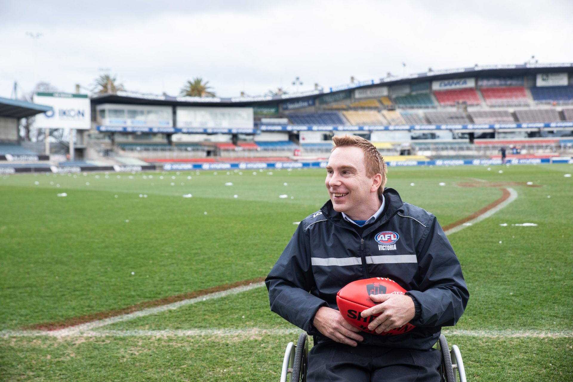 Man in a wheelchair holding a football at a football stadium.