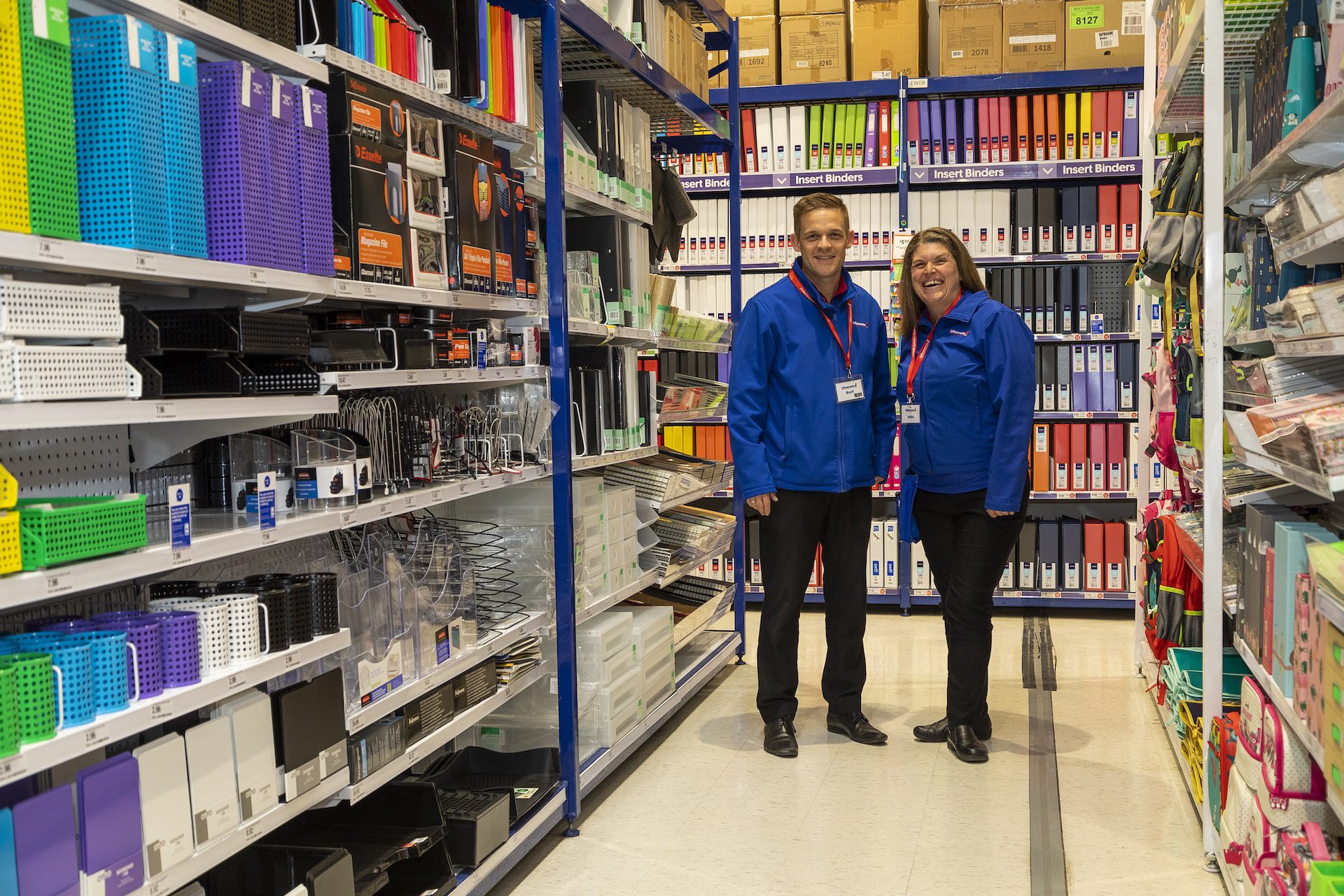Male and female clerks standing in an office supplies aisle.