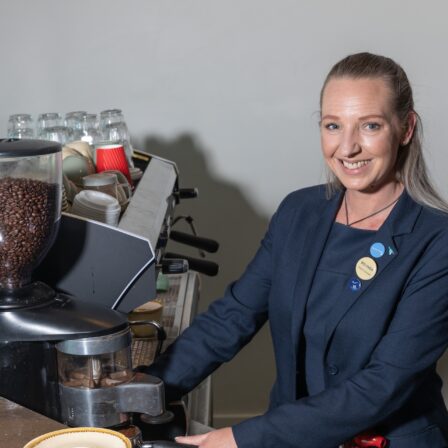 Woman smiling as she stands beside a coffee machine.