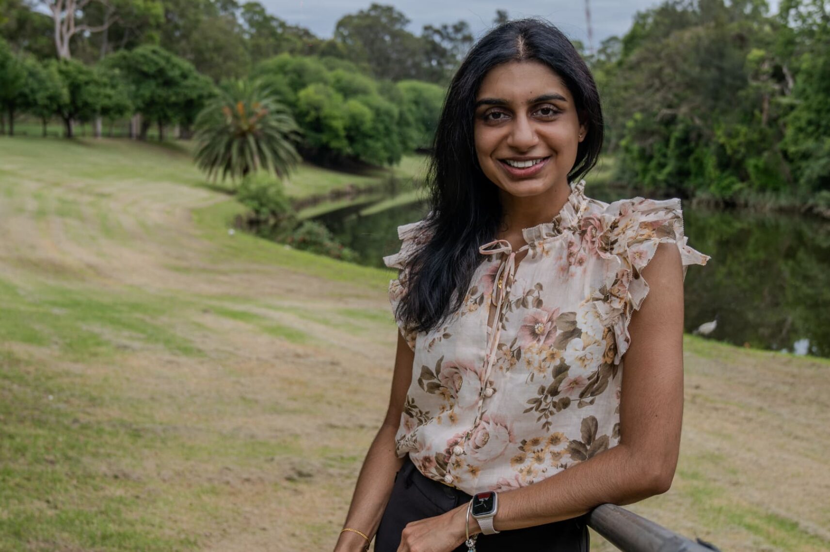 Prakasca wearing a white blouse, smiling and standing in front of a green garden