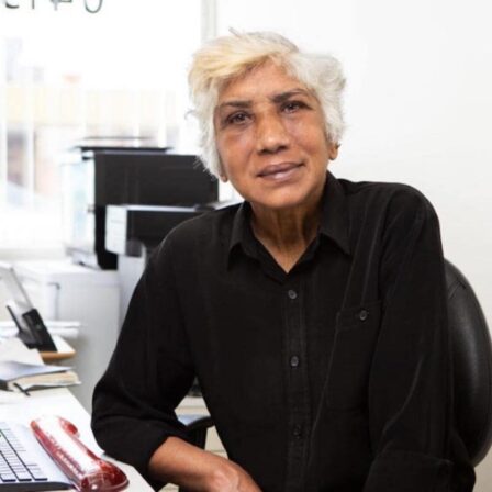 An elderly woman with white hair, sitting by her office desk.