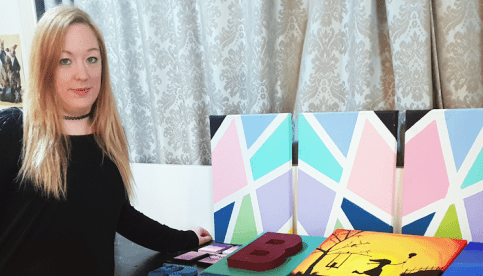 A young womanstanding beside a colorful artwork.