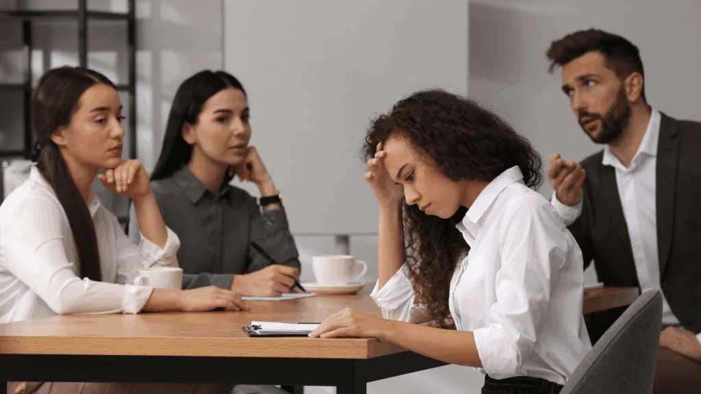 Three office workers staring judgingly at a self-conscious female colleague.