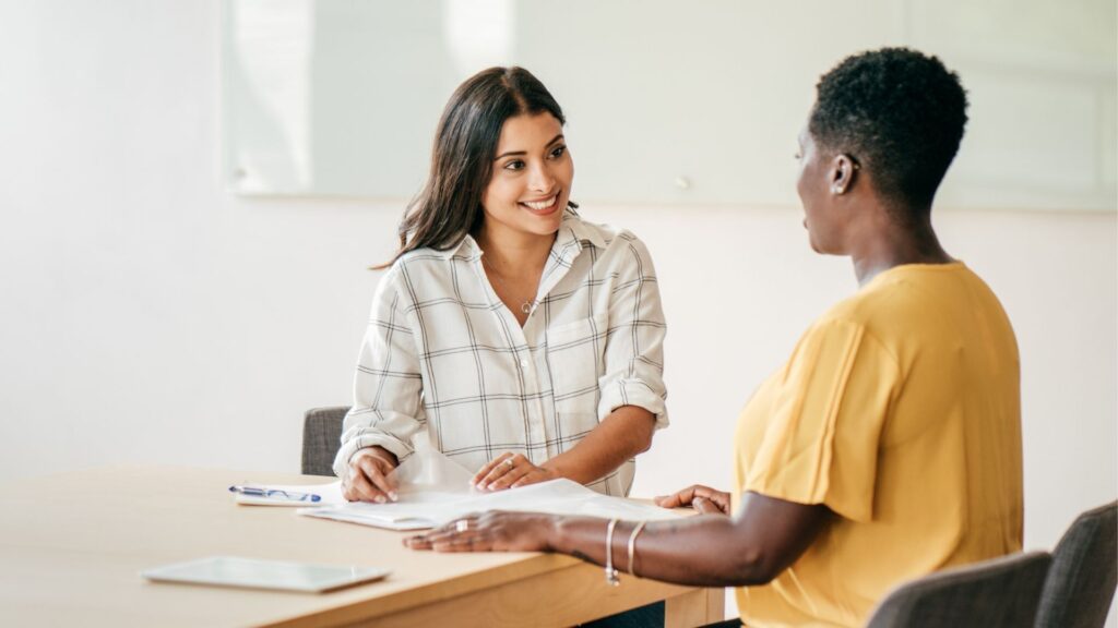 Two women talking while seated at a conference table.