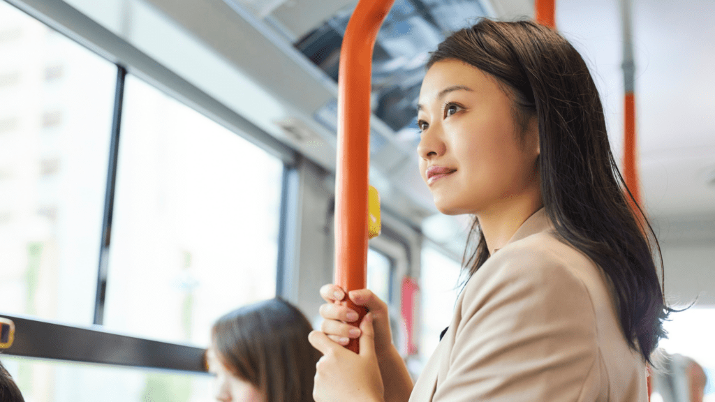A woman standing on public transport, holding a handrail and looking out the window.