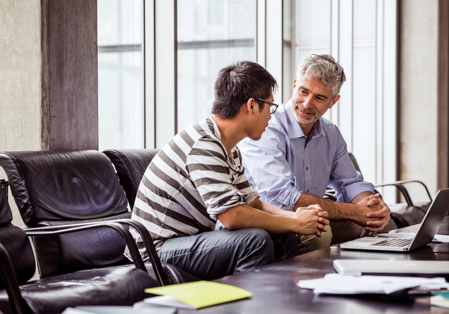 Middle-aged man speaking with a younger man in an office meeting room.